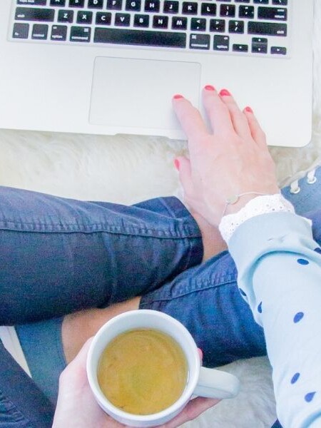 Image of Sarah sitting crossed legged using macbook and holding a cup of tea