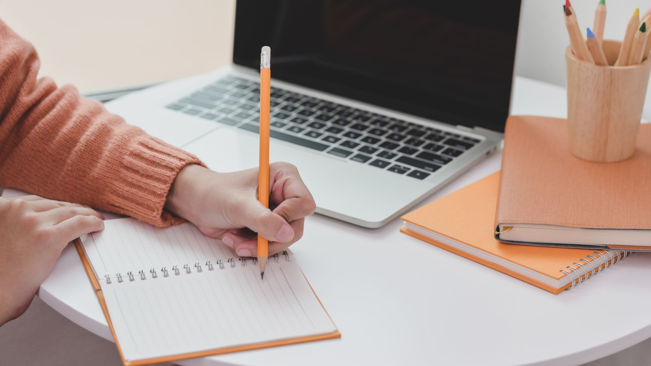 Image of woman writing in notebook with laptop in background - sarah RIchards Social