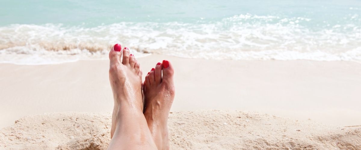 Image of feet with painted toes on beach with waves lapping the shore