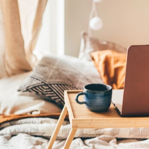 Image of a bed with a tray containing laptop and coffee mug