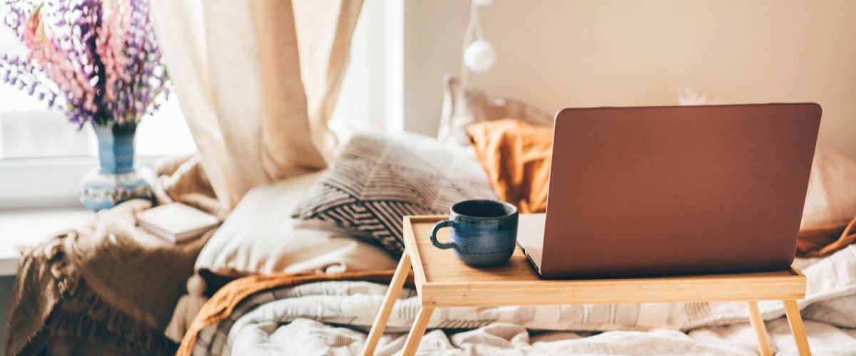 Image of a bed with a tray containing laptop and coffee mug