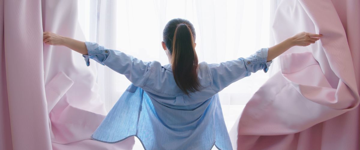 Image of woman opening her curtains widely - a let's do this action